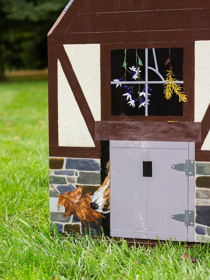 painted dog house depicting garage door and flowers hanging behind a window